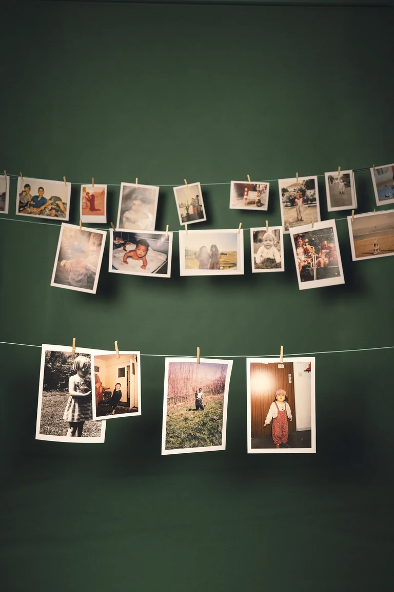 Viele Fotos hängen an zwei gespannten Schnüren vor einer grünen Wand. Sie sind mit kleinen Klammern befestigt.