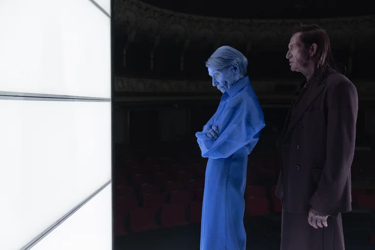 Zwei Personen stehen vor einem leuchtenden Bildschirm. Eine Figur ist blau und transparent, die andere trägt einen dunklen Mantel.