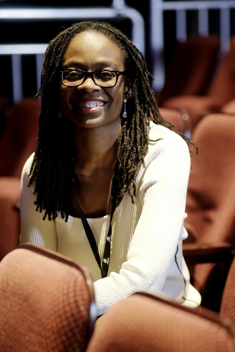 Eine Person mit Brille und Dreadlocks sitzt in einem Theatersitz. Sie lächelt freundlich in die Kamera.