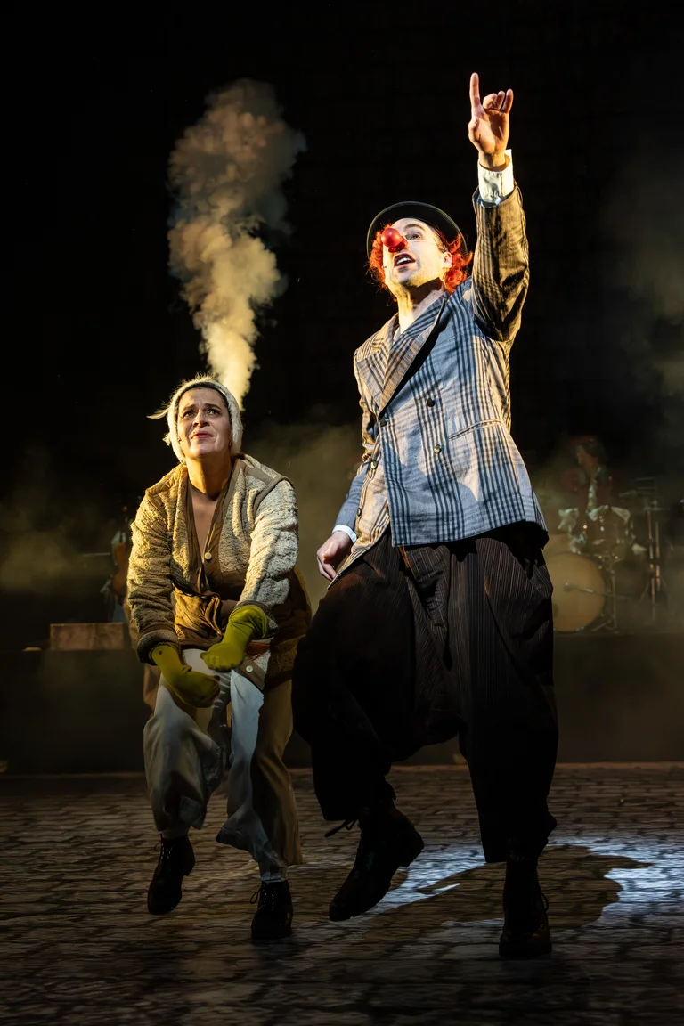 Zwei Schauspieler auf der Bühne, einer mit rotem Haar und Vintage-Outfit. Der andere hat eine Wolke hinter sich.